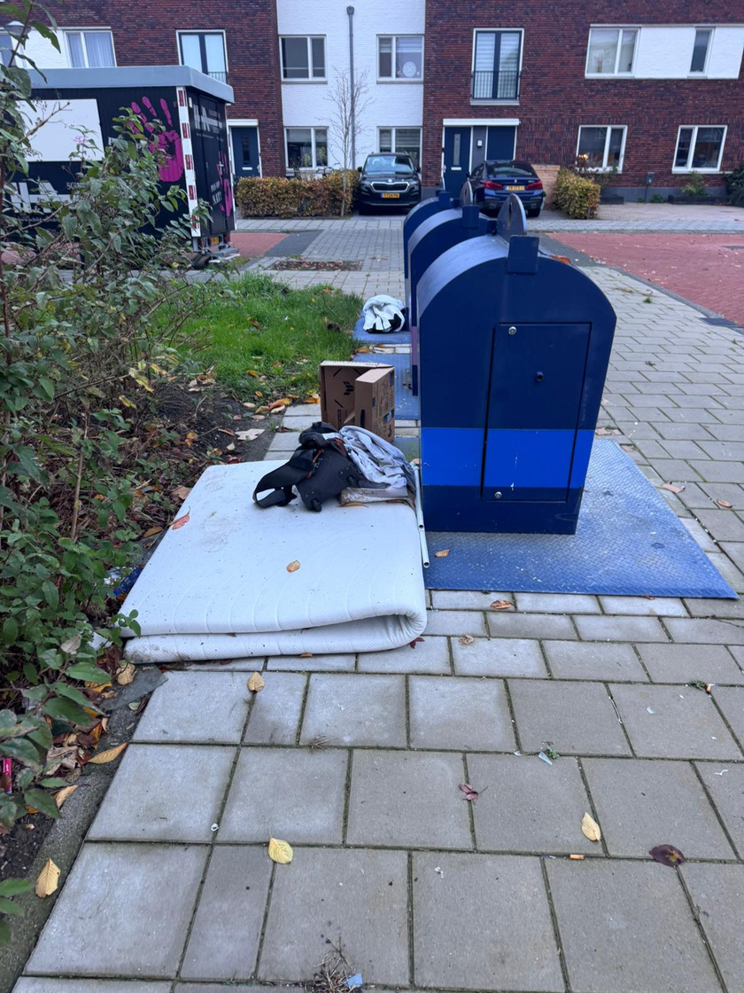Matras en afval gedumpt naast een ondergrondse container in een woonwijk